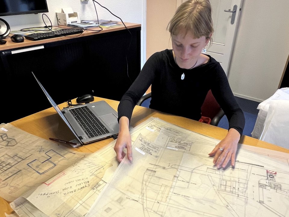 Een dame is bezig met oude molen tekeningen beschrijven en bekijke. Naast haar staat een laptop op het bureau..