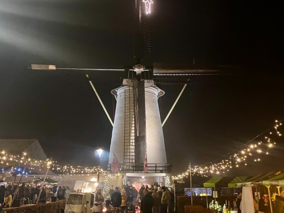 Avondfoto van de witte molen in Borlen en schaft met kerstster op de wieken. en daarvoor marktkraampjes