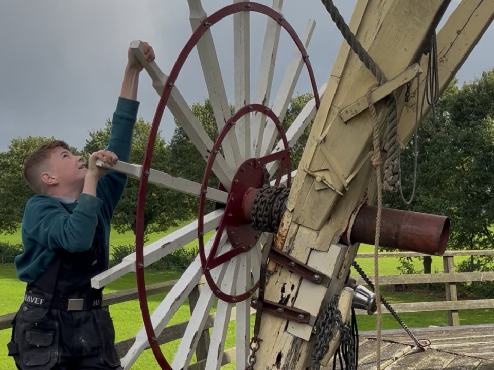 Jonge jongen op de stelling van molen, draait aan het kruiwiel van de molen om deze op de wind te zetten.