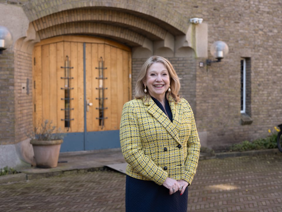 culinair journalist en presentator Janny van der Heiden staat lachend voor een deel van een oud pand