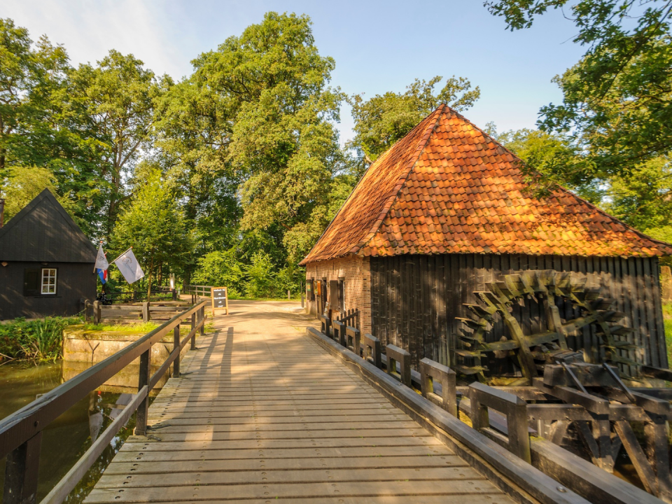 beeld vanaf een bruggetje met aan de rechterkant de Noordmolen (watermolen) en de linkerkant een gebouwtje. Zon straalt mooi op de watermolen